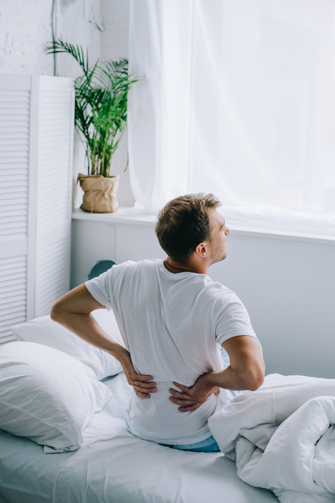 Man sitting on bed experiencing lower back pain